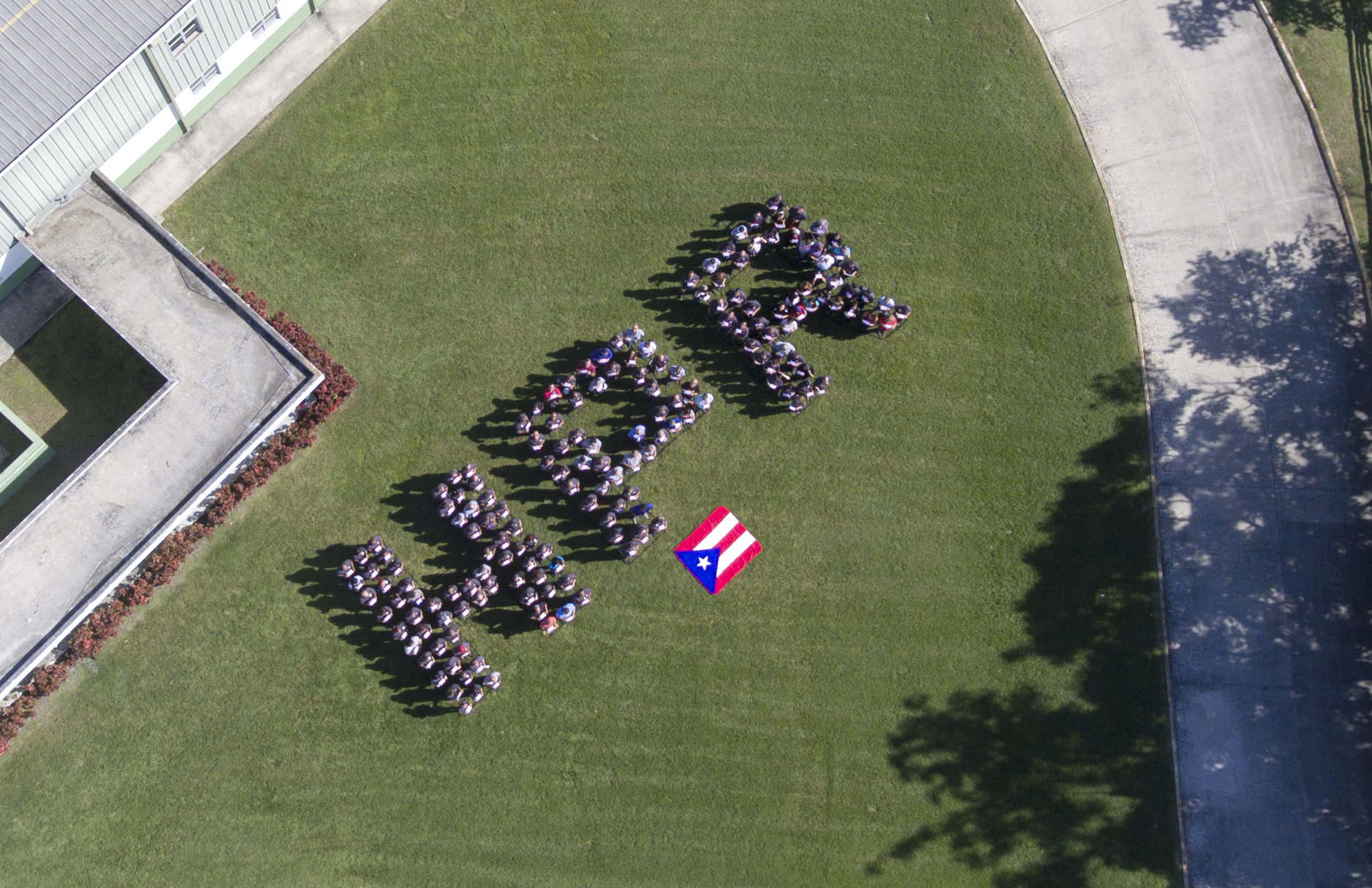 An aerial view of people lined up to spell out the letters HPA in front of a Puerto Rican flag.