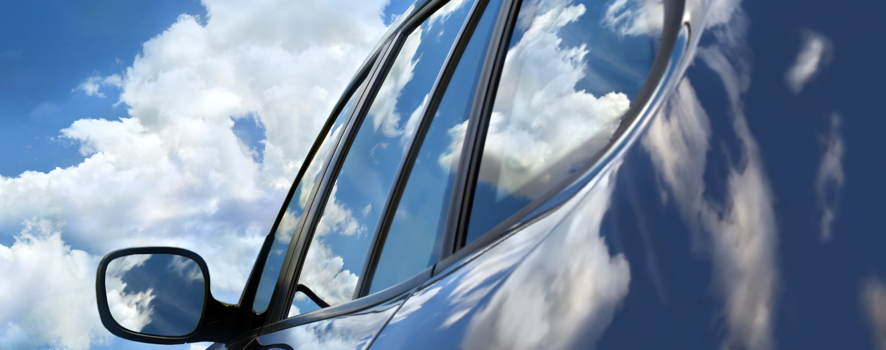 A car with sky and clouds reflecting on surface