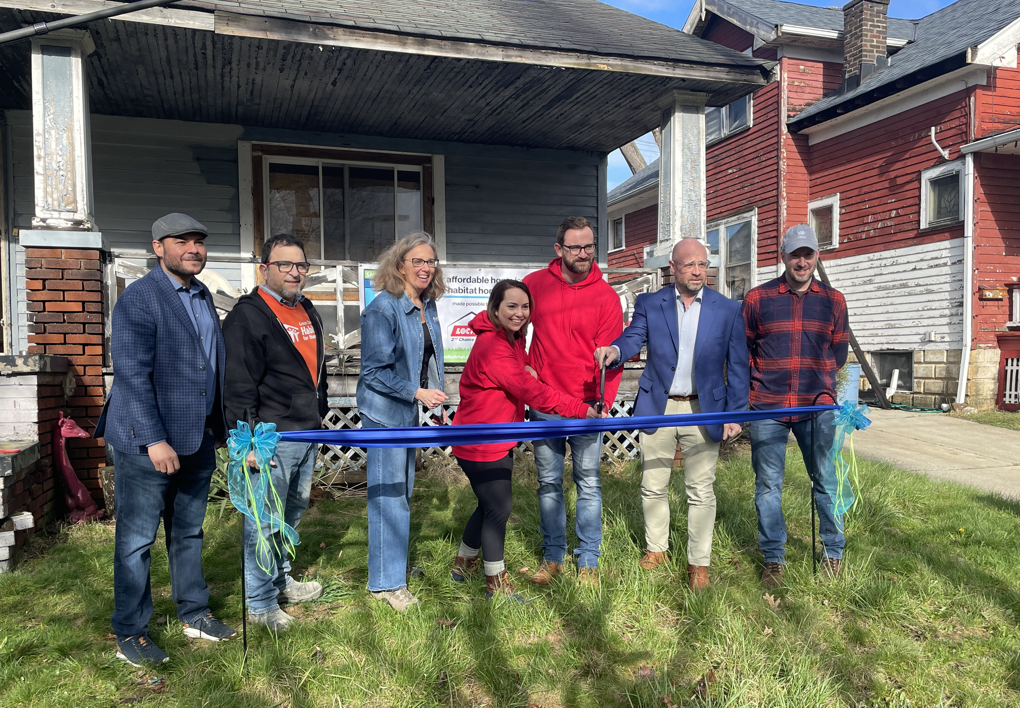 Group of people in front of house cutting ceremonial ribbon.