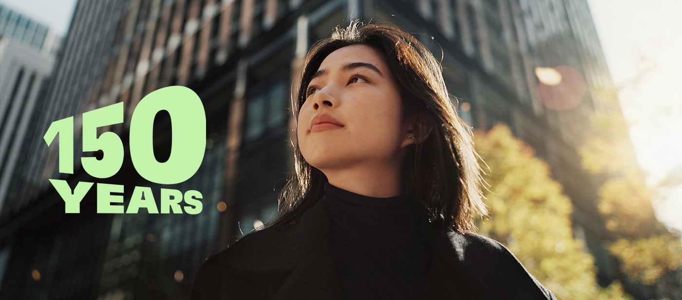 绿色文字“150 YEARS”置于现代城市景观之上，背景为高耸的玻璃建筑与秋色树木，象征着汉高150周年的庆祝标志。