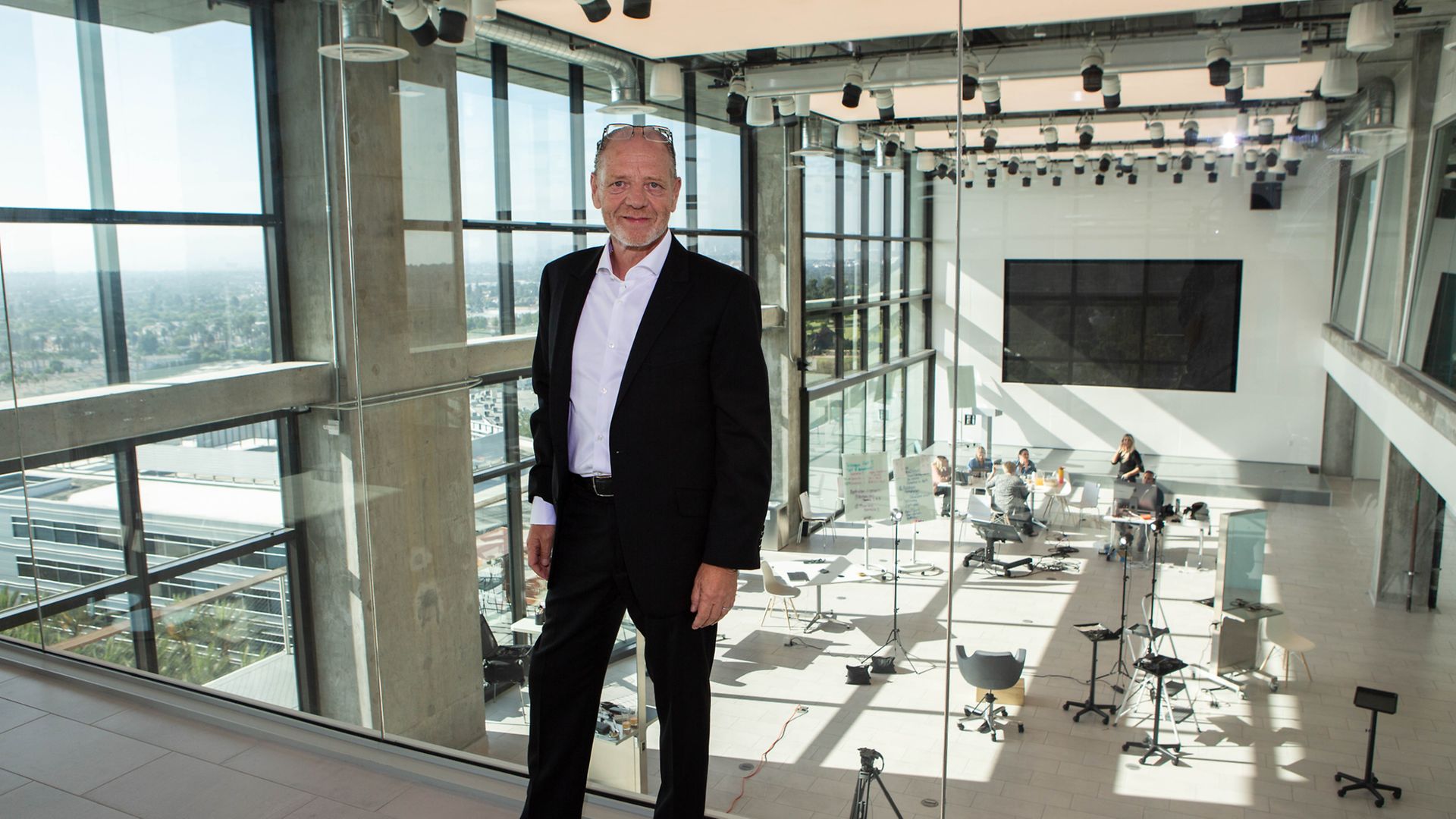 Stefan L. Mund, Regional Head Henkel Beauty Care Professional North America in front of a glass wall with view of a seminar room with people