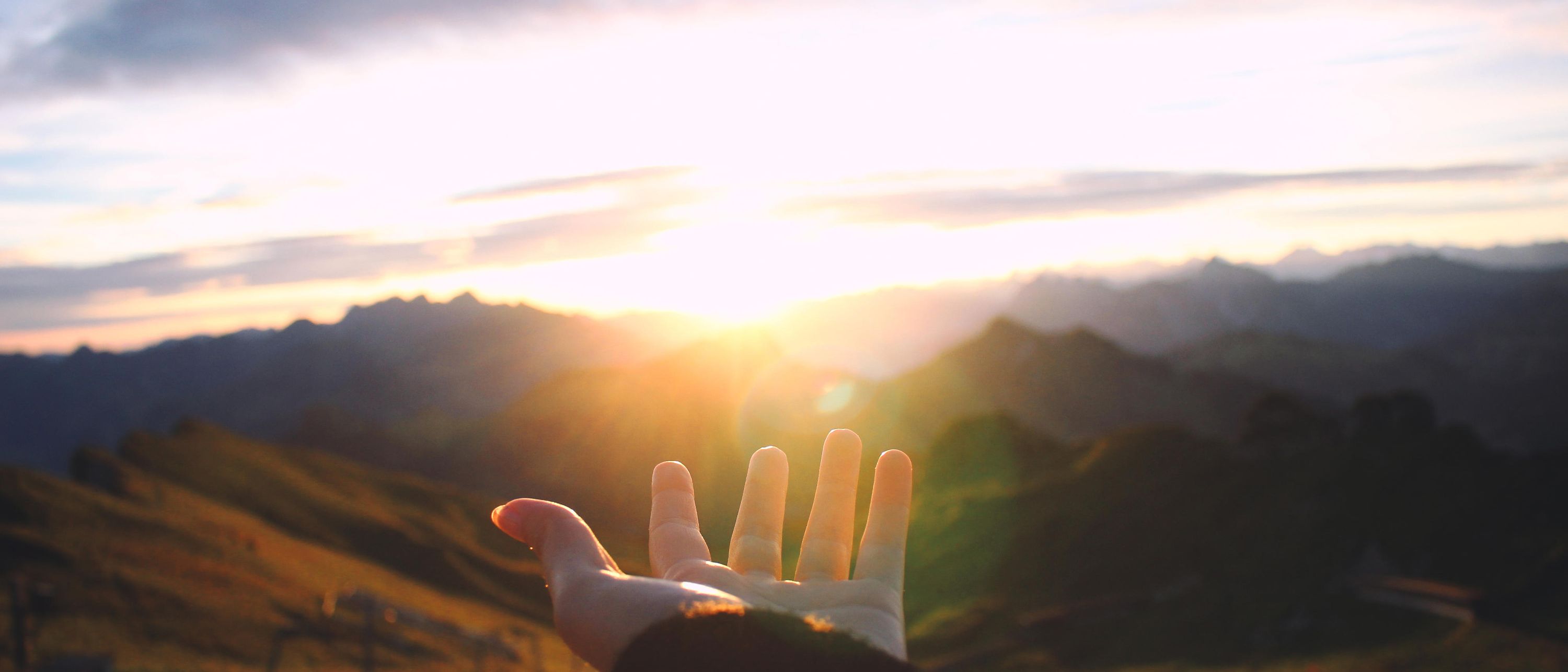 Hand reaching out towards the sunrise