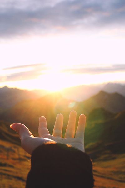 Hand reaching out towards the sunrise