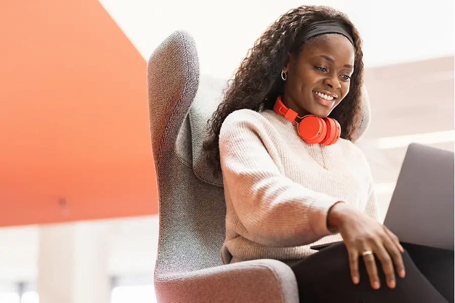 A Henkel employee sits in a comfy chair with her laptop on her knees. She smiles.