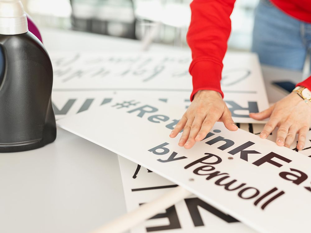 Signs with the inscription #rethinkfashion by Perwoll lie on a table and get sorted by two hands.