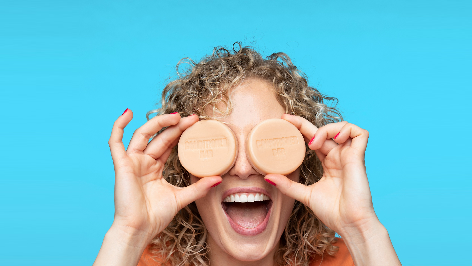 A happy woman holds two Nature Box solid conditioners in front of her eyes.