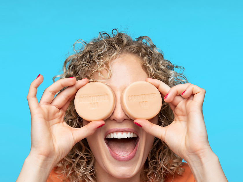 A happy woman holds two Nature Box solid conditioners in front of her eyes.