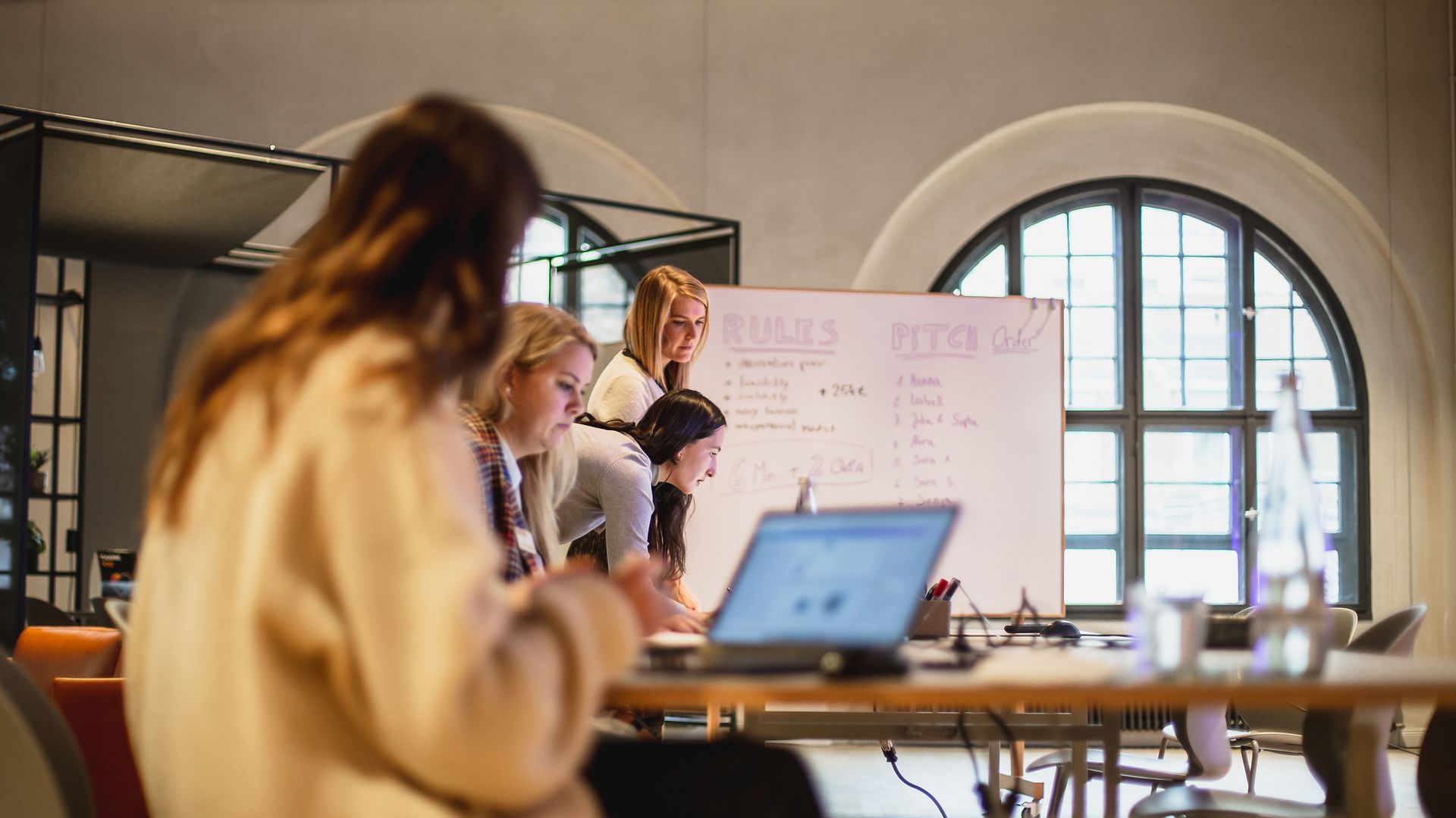 Women work on laptops in front of a flipchart.