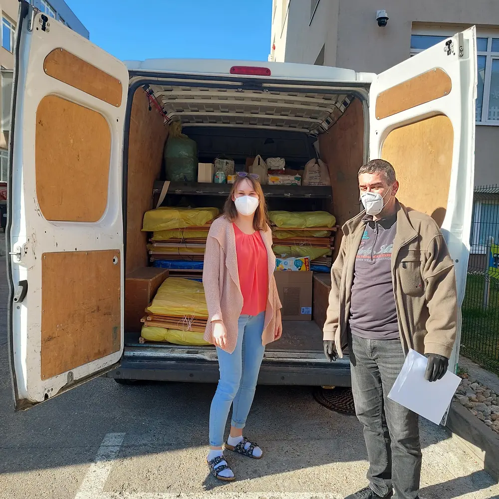 A woman and a man standing in front of a van loaded with cribs and mattresses that are being donated.