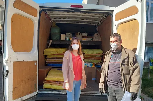 A woman and a man standing in front of a van loaded with cribs and mattresses that are being donated.