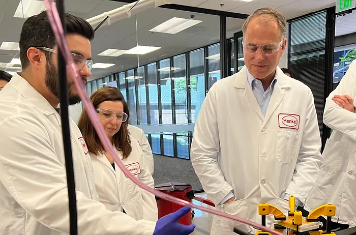 Jan-Dirk Auris (pictured right), Henkel Executive Vice-President Adhesive Technologies, observes a color-matched adhesives demonstration from Application Engineers Efren Jimenez and Burcak Conley