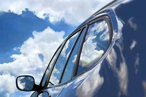 A car with sky and clouds reflecting on surface