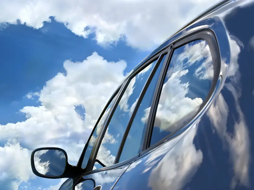 A car with sky and clouds reflecting on surface