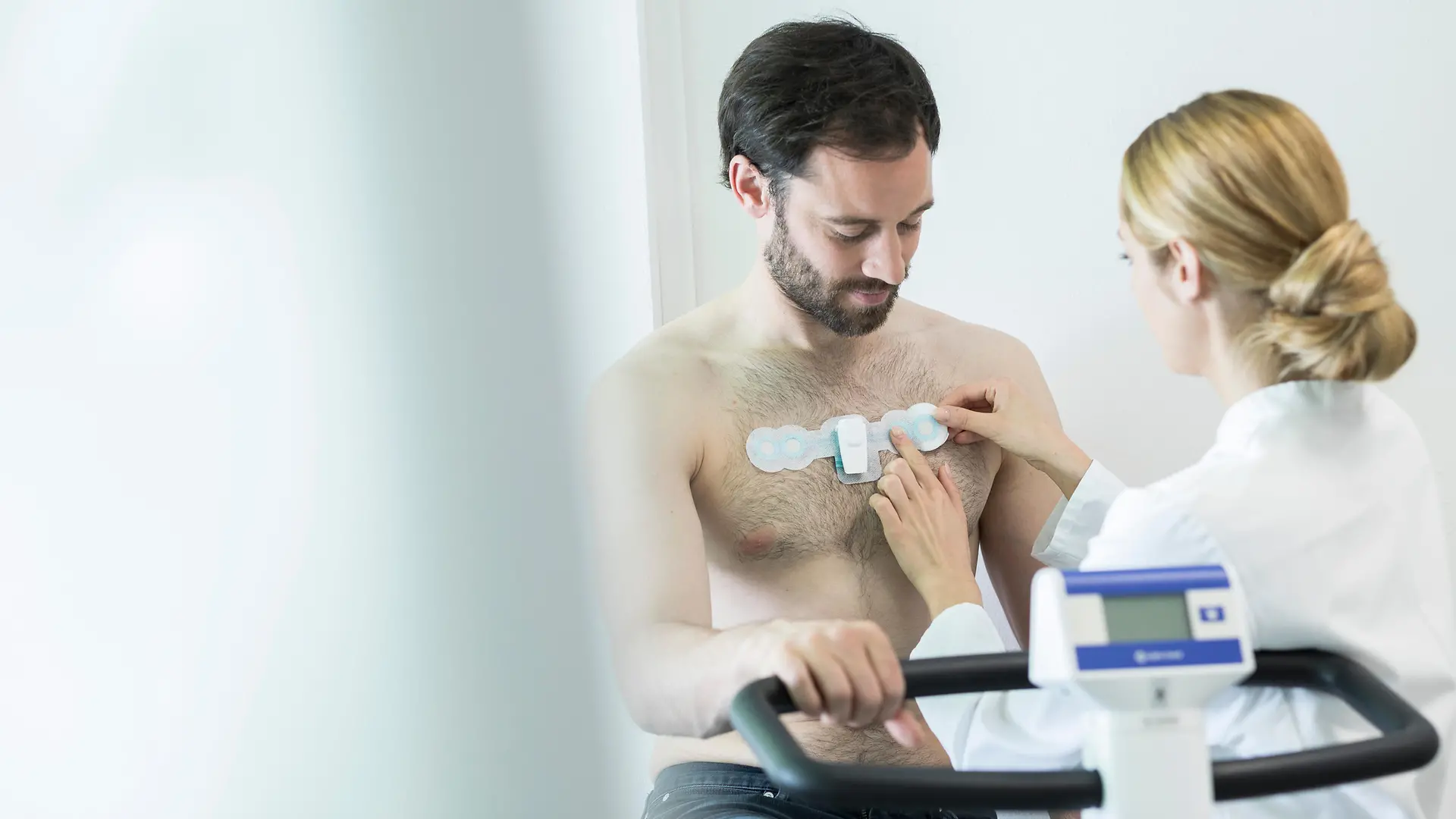 A female doctor on the right applies a smart patch to a man’s chest to perform a medical exam.