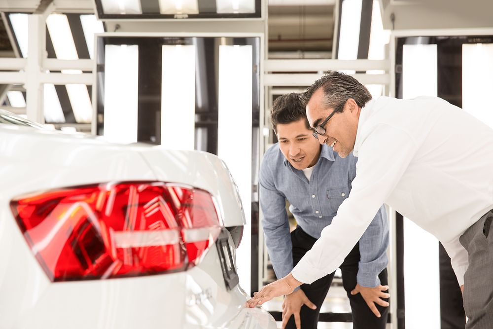 Two men are examining the backside of a white car.