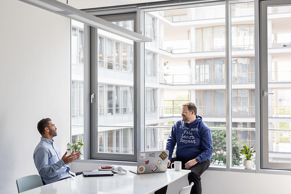 Two young men in a light office space talking in a relaxed atmosphere.