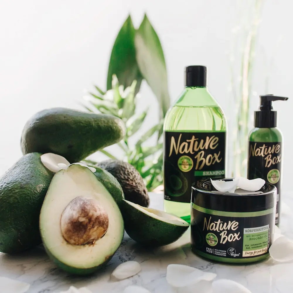 Three Nature Box products are standing next to some avocados. 