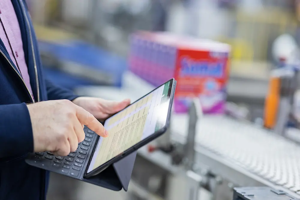 A man is using a tablet while standing next to an assembly line.