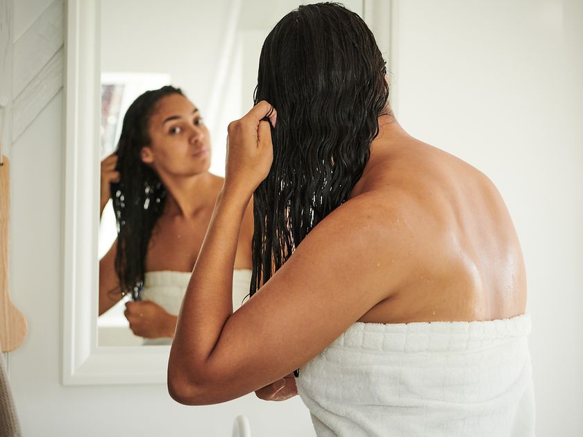 A woman stands in front of the mirror with a bath towel and wet hair.