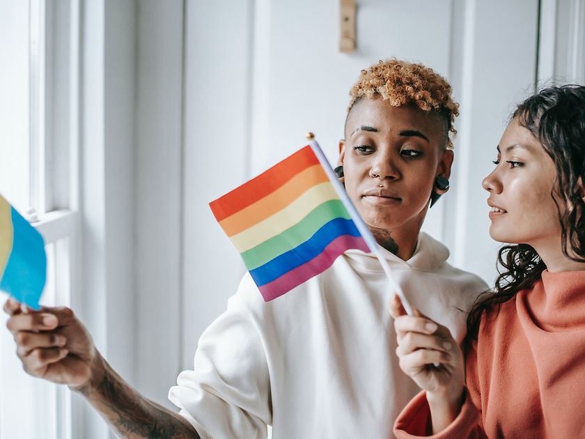 Two women are talking to each other while holding an LGBTQ+ flag.