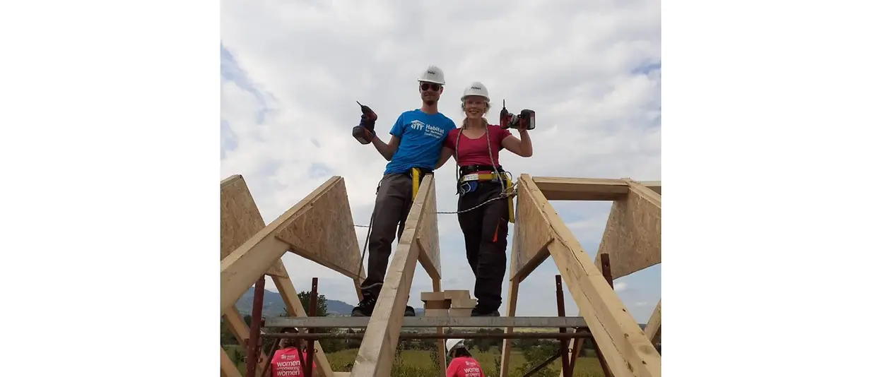 Two helpers stand on the wooden scaffolding and pose for the photo, holding their drills aloft.