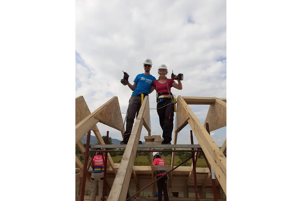 Two helpers stand on the wooden scaffolding and pose for the photo, holding their drills aloft.