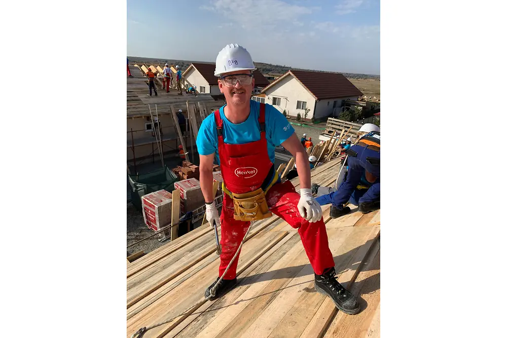 Secured with a belt, Henkel employee Jörg stands on the roof of the unfinished apartment building.