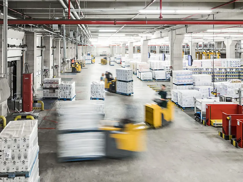Forklifts move pallets in a production hall.