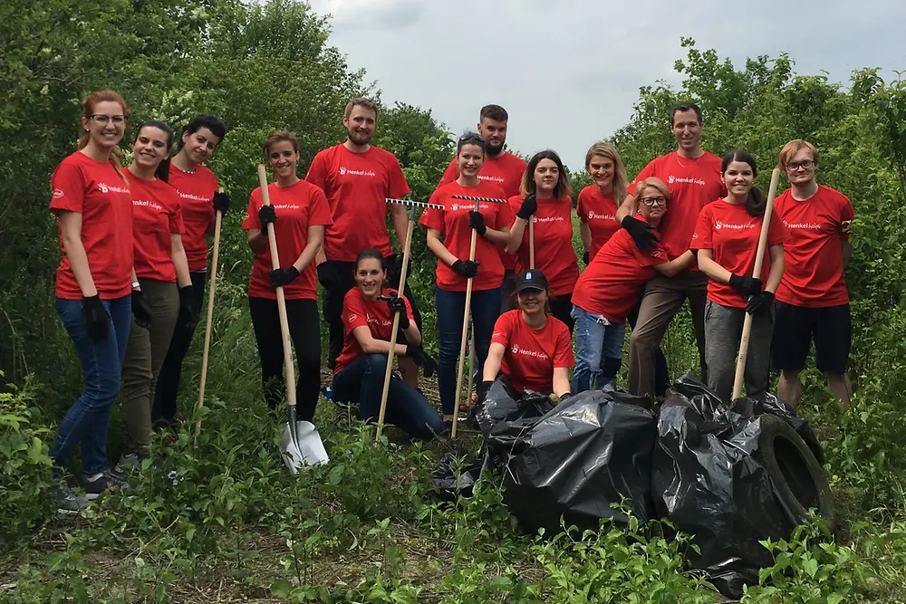Henkel employees in red trashfighter t-shirts are standing in nature; there are two full garbage bags in front of them.