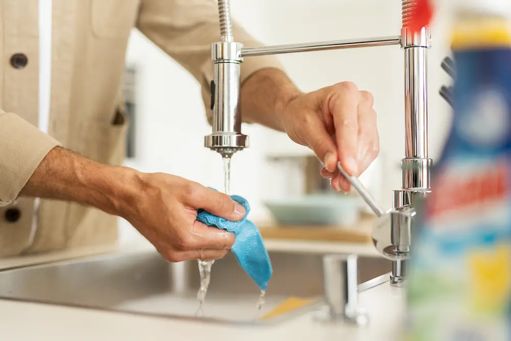 A man is standing at the sink rinsing a rag.