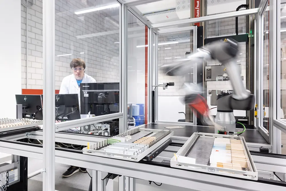 In an automated lab, a robotic arm works on new adhesive solutions.