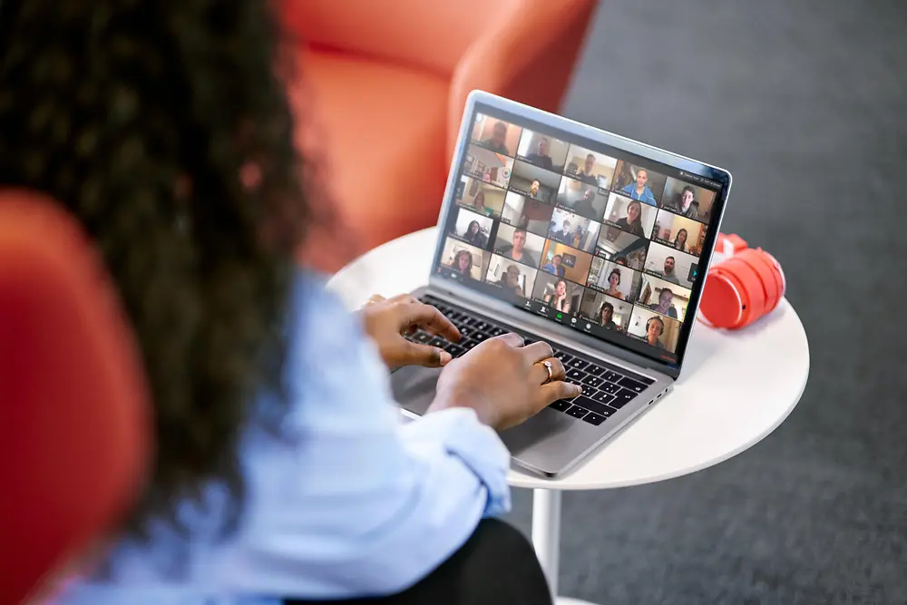 An employee sits at a table and participates in a digital gathering with her colleagues on her laptop.