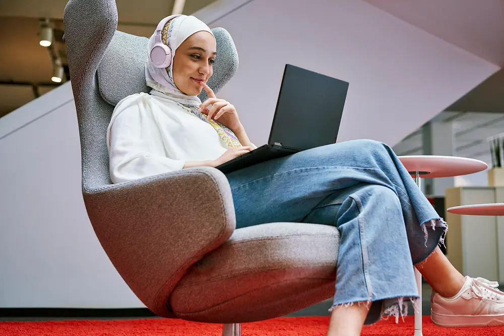 An employee sits in an armchair and looks at the screen of her laptop.