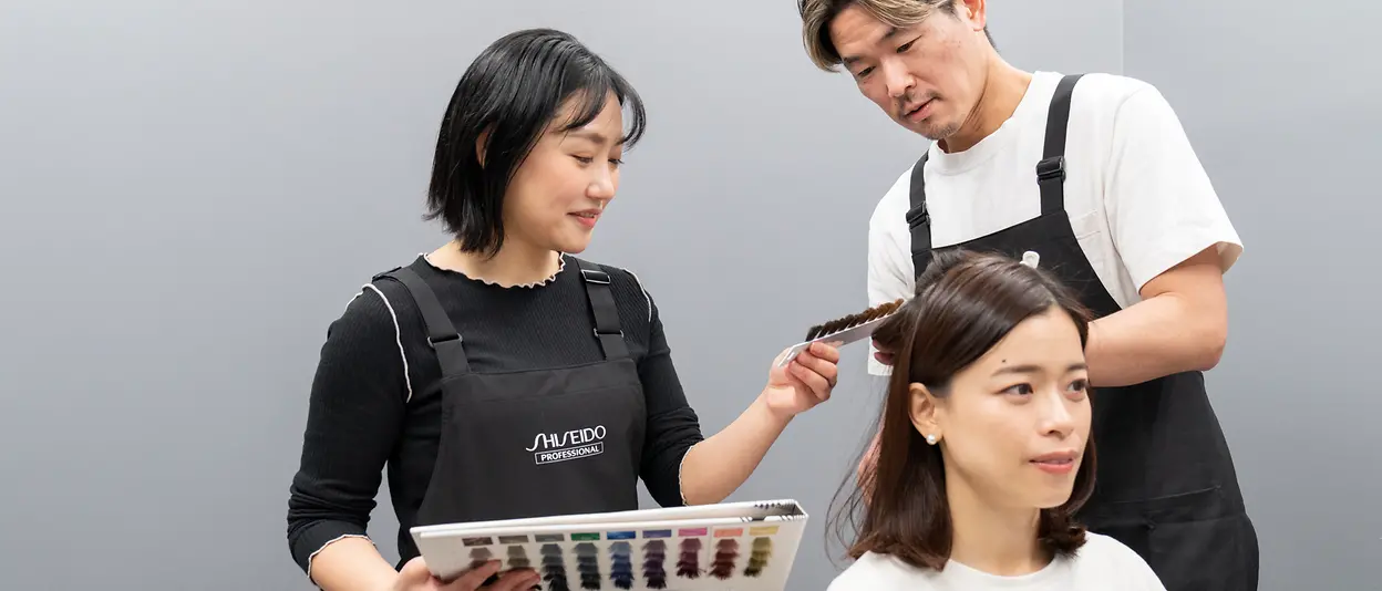 Two hair care professionals perform a hair color analysis on a consumer.
