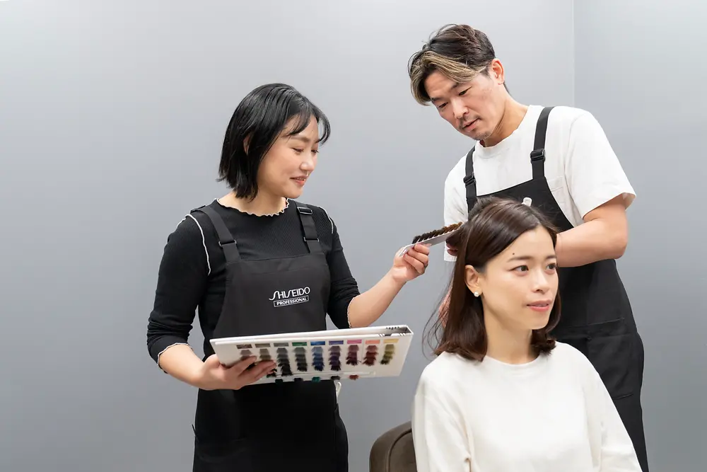 Two hair care professionals perform a hair color analysis on a consumer.
