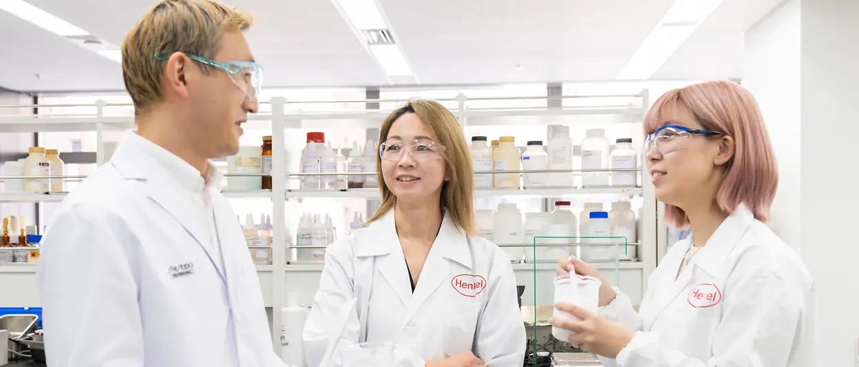 Three researchers stand in a hair care R&D lab and speak to each other.