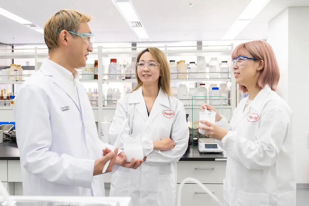 Three researchers stand in a hair care R&D lab and speak to each other.