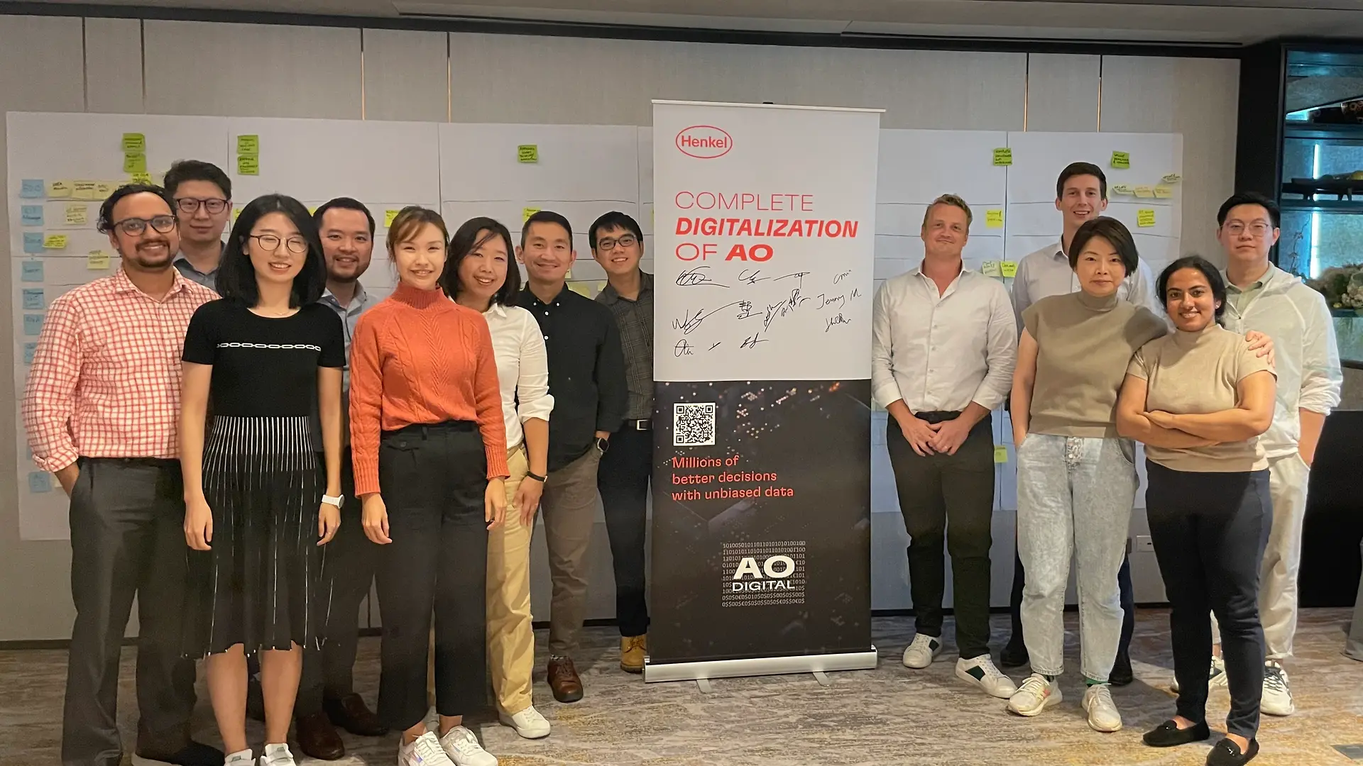 Nick and his team stand together in a meeting room posing next to a roll-up that says “Complete Digitalization of AO”.