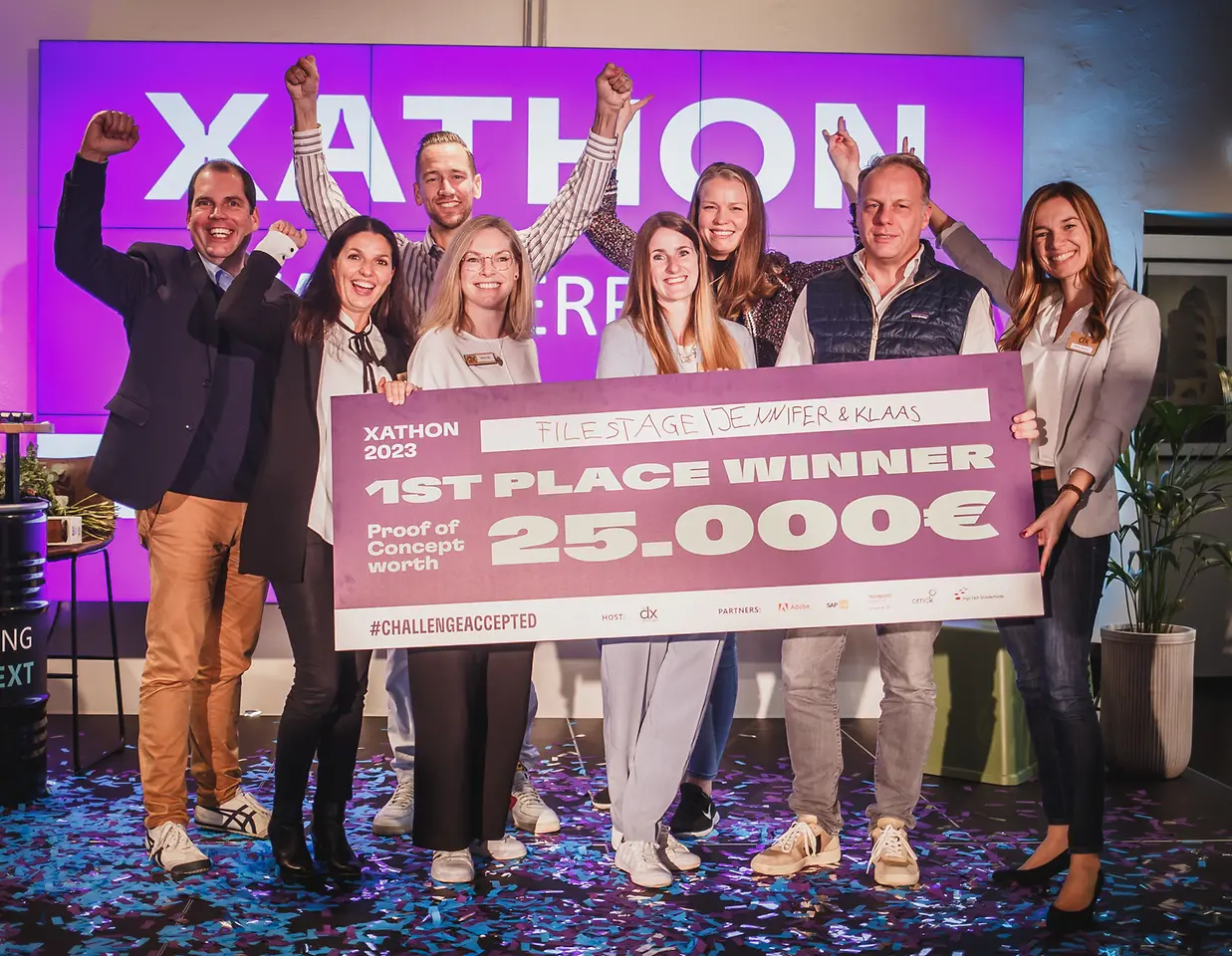 Three men and five women standing on stage cheering and holding a cheque saying 