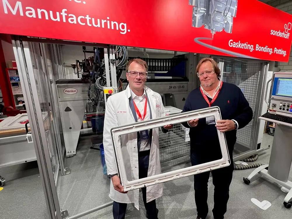 
Harald Dekkers, Dometic Product Area Manager for Windows, Blinds, Doors & Sanitary and Peter Fischer, Henkel Senior Manager Market & Customer Activation, present a Dometic window frame sealed with PU foam, standing in front of the Sonderhoff mixing and dosing system in Henkel's ICD laboratory (Düsseldorf).
