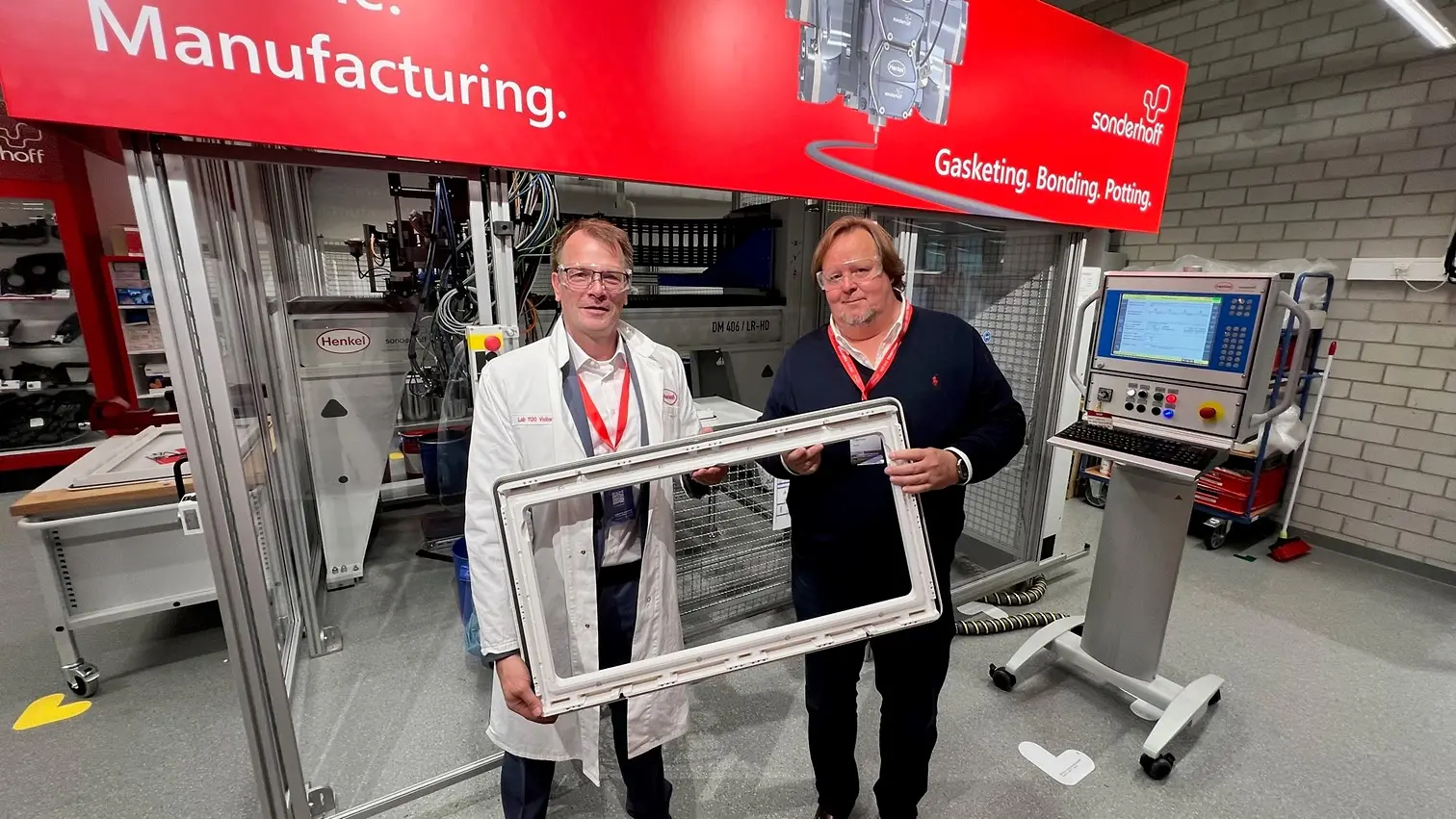 
Harald Dekkers, Dometic Product Area Manager for Windows, Blinds, Doors & Sanitary and Peter Fischer, Henkel Senior Manager Market & Customer Activation, present a Dometic window frame sealed with PU foam, standing in front of the Sonderhoff mixing and dosing system in Henkel's ICD laboratory (Düsseldorf).
