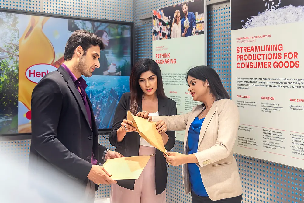 A customer experience tour guide presents application examples from Henkel Adhesive Technologies to two customers at the Technology Center Mumbai.