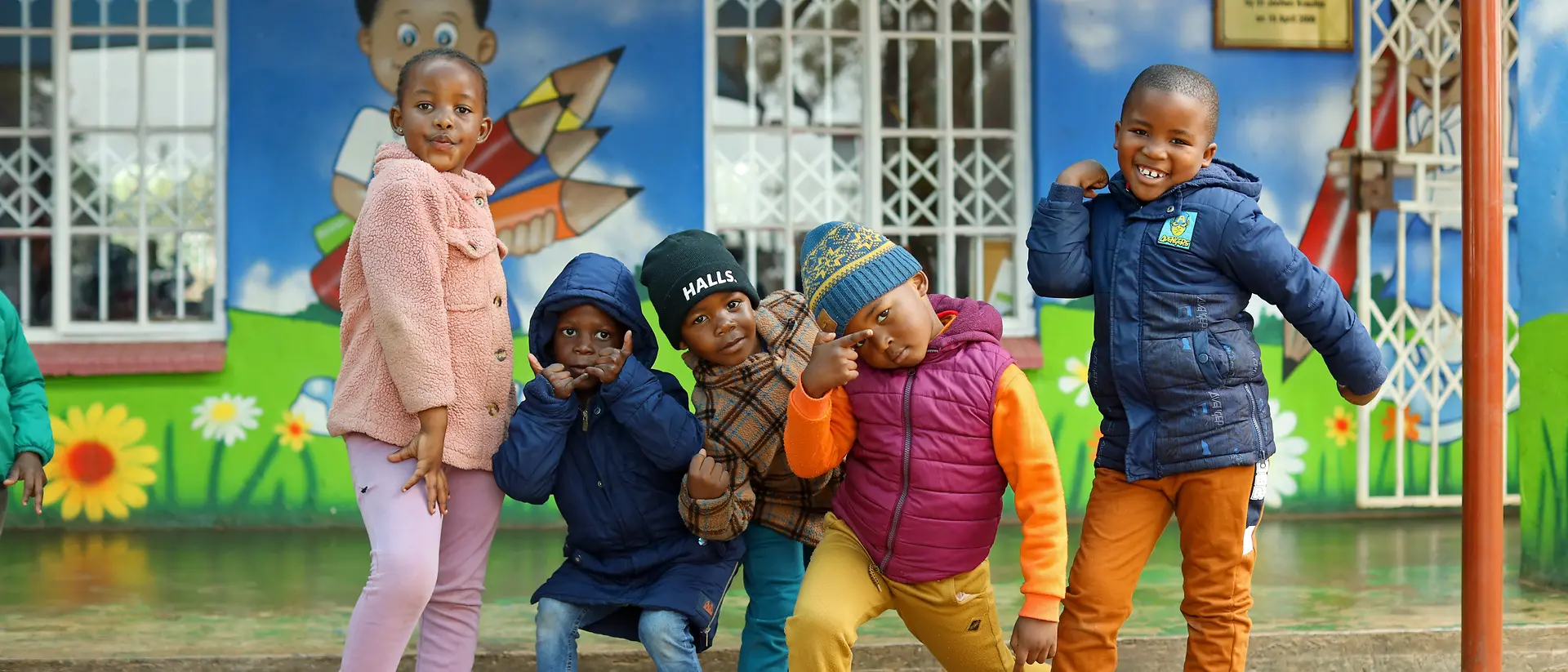Five children stand next to each other in colorful clothes and make funny poses.