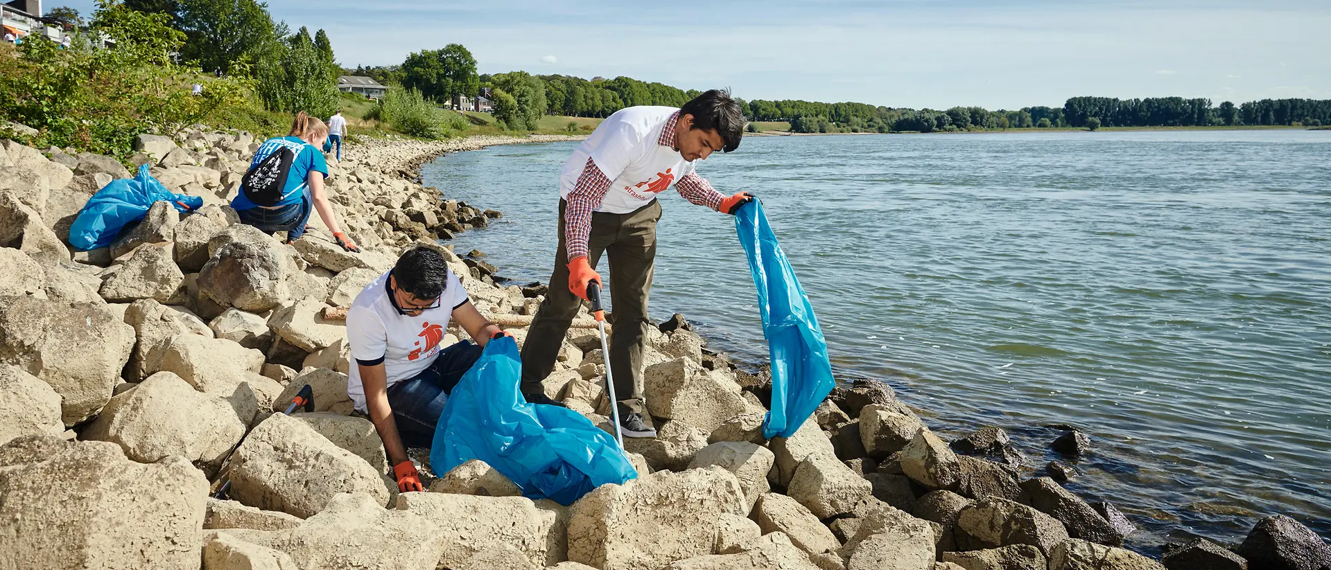 A group of volunteers collects thrash with waste pickers during a thrash collection event on a riverbank.
