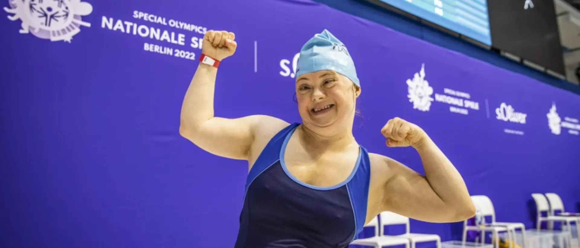 A swimmer taking part in the Special Olympics looks into the camera, smiling and cheering.