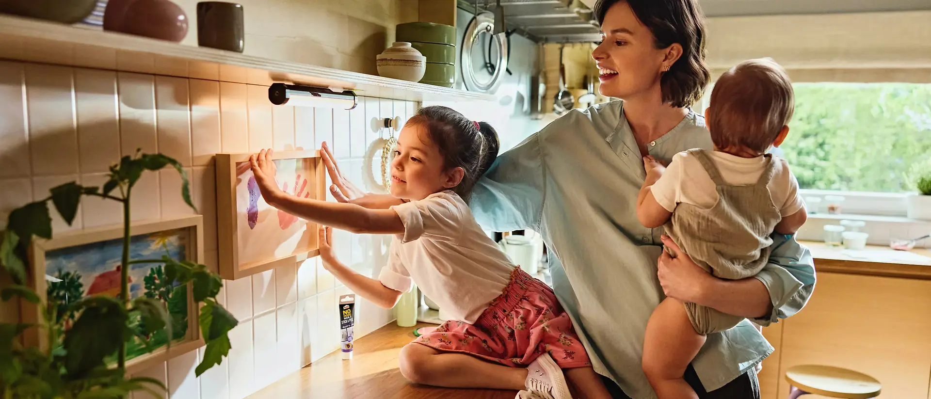 A mother and her daughters hang a picture on the wall using Pattex Stick and Peel.