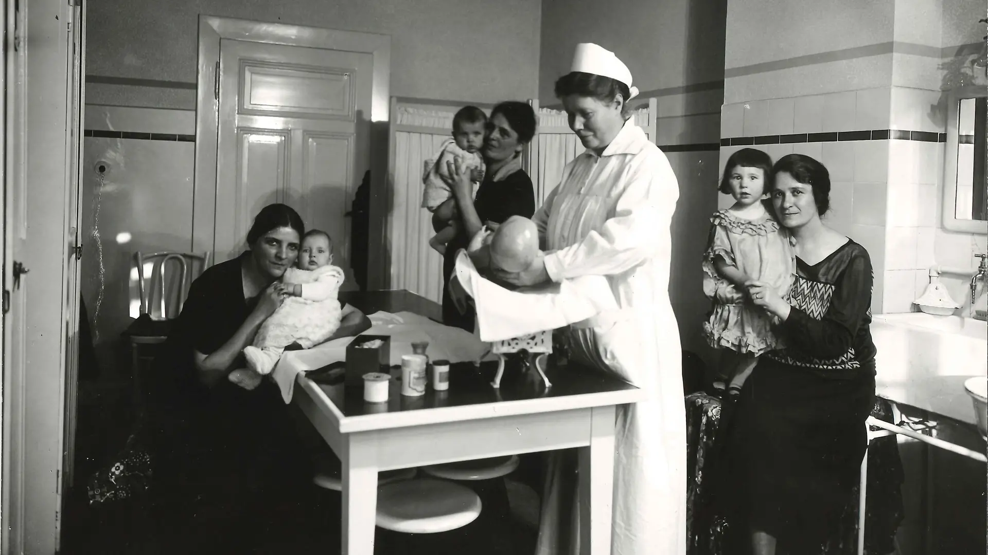 Henkel nurse examining an infant and three mothers with their infants.