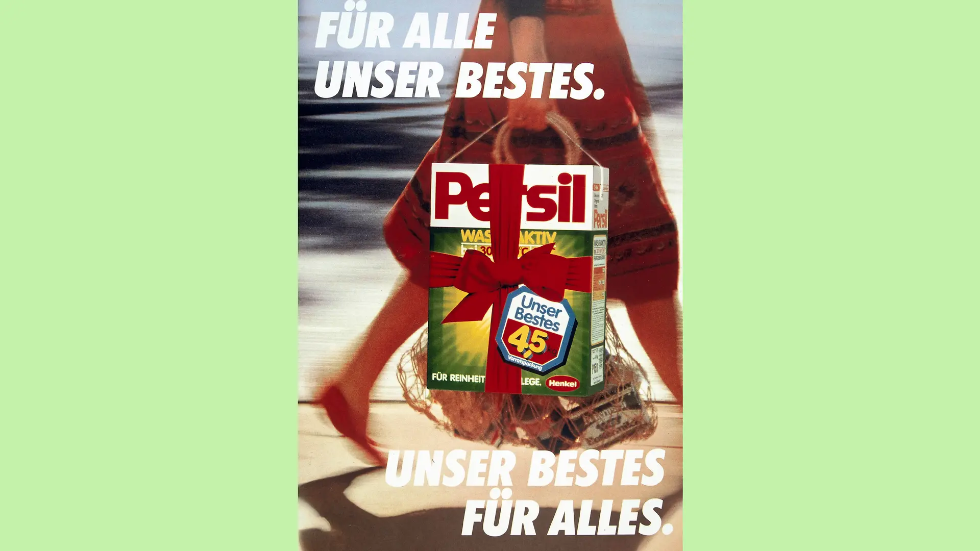 Advertising poster for the Our Best campaign. The background consists of a painted blurred image of a woman walking down the street with her shopping in her hand. The image shows the woman only up to her hips. She is wearing a red skirt and red shoes. In the foreground of the motif is a packet of Persil with a red ribbon tied around it. It is placed in such a way that it gives the impression that the woman in the background is holding the package together with her other items. In the top left-hand corner, the slogan 