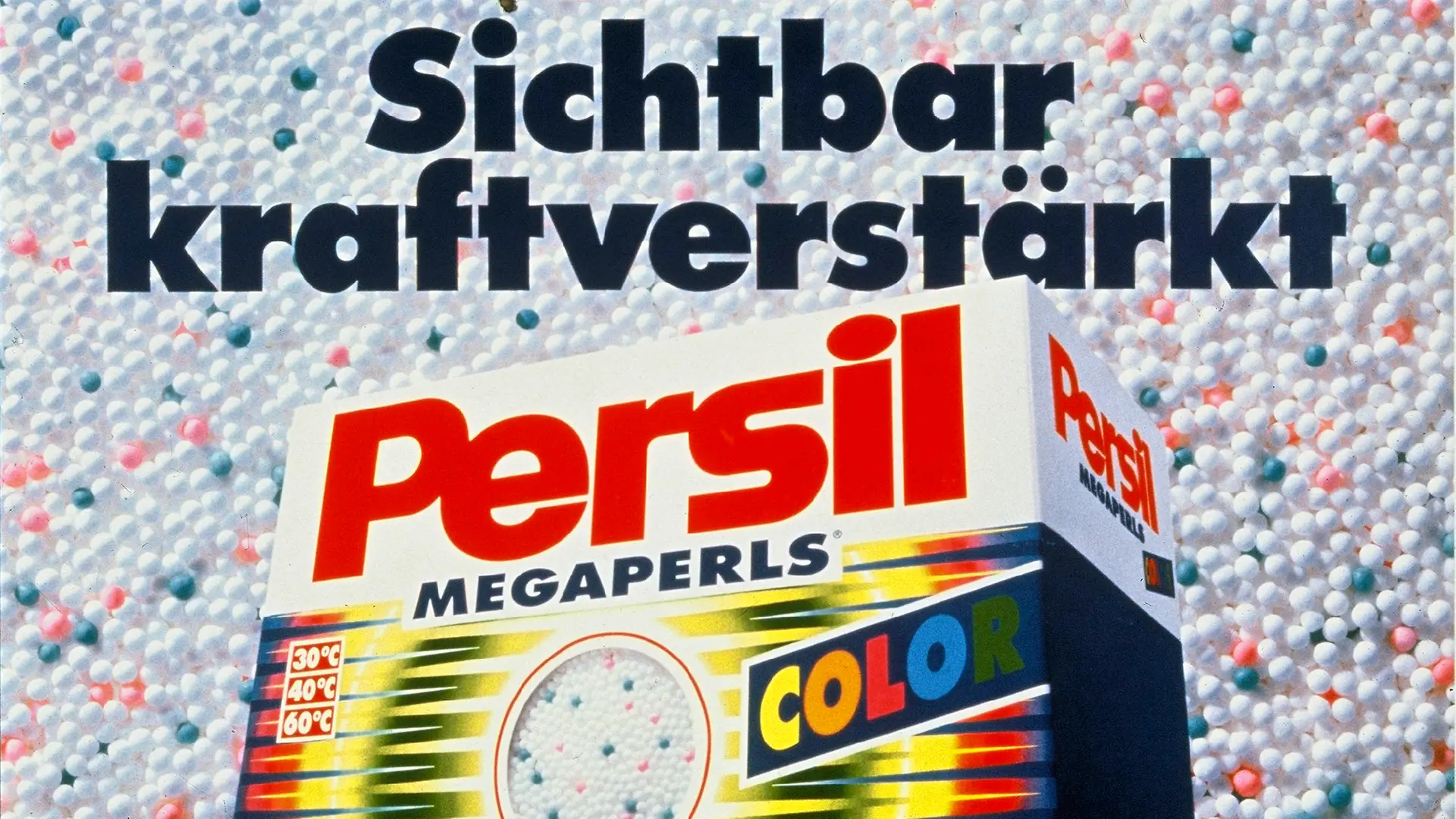 A pack of Persil Color Megaperls lies on a bed of colorful Megaperls - the spherical washing powder from Henkel. At the top of the advertisement it says: “Visibly strength-enhanced”.