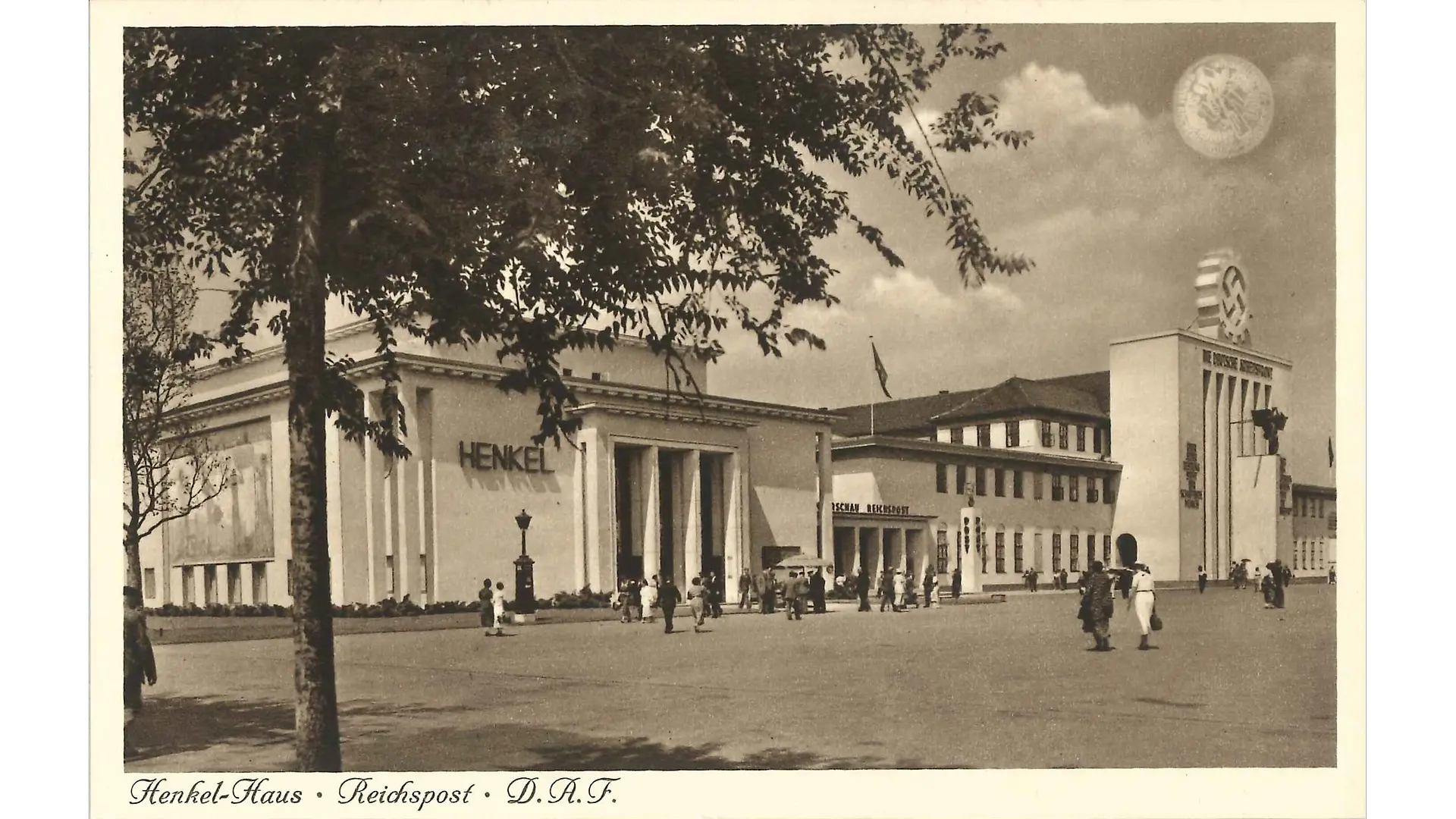 The Henkel Pavilion at the Reich Exhibition “Schaffendes Volk” (“Working Nation”). Although the architectural style is rather simple, the building appears very magnificent due to its enormous size and the tall pillars integrated into the facade – especially when compared to the rather small-looking building next to it. The company name Henkel is displayed prominently to the left of the main entrance.
